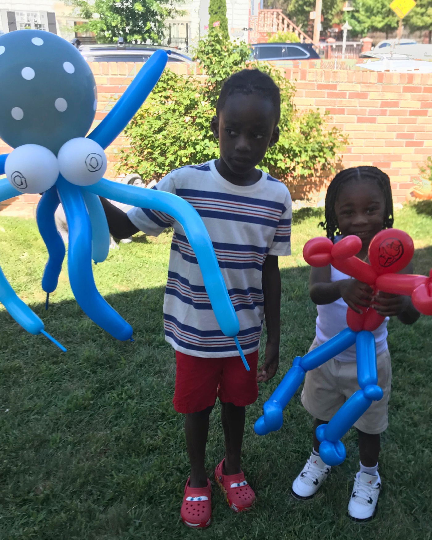 Two children outdoors proudly holding colorful balloon animals