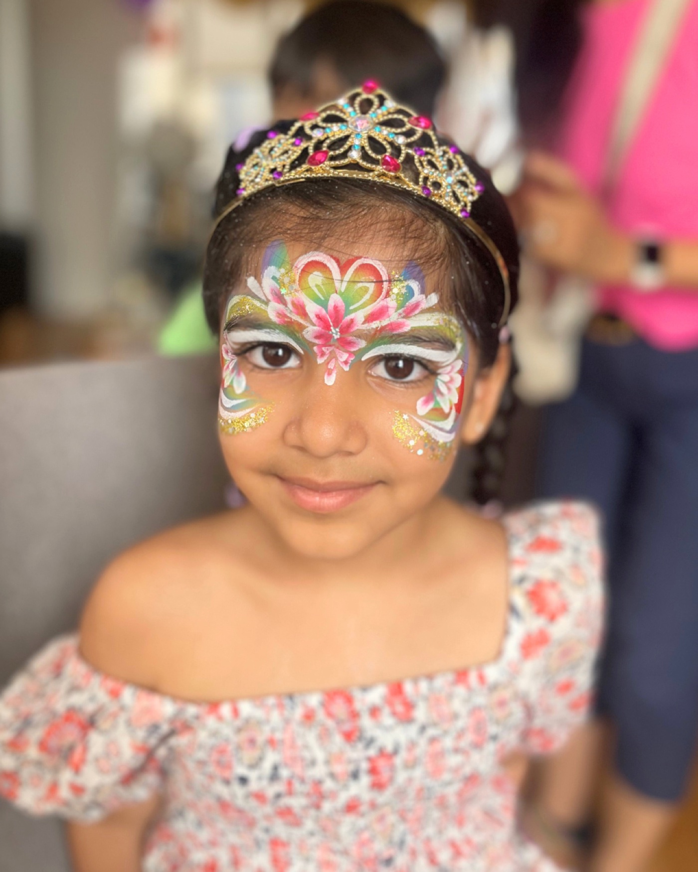 Smiling child wearing a jeweled tiara with an elaborate floral princess face-paint design