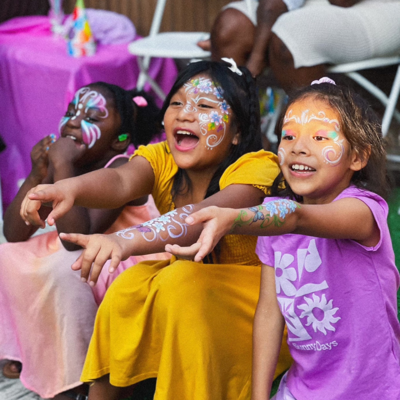 Three children laughing together with colorful face paint at a real party
